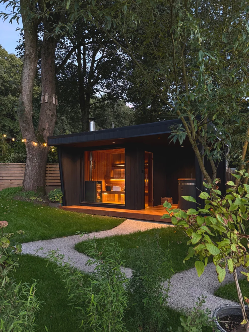 Warmly lit sauna set among trees and planting