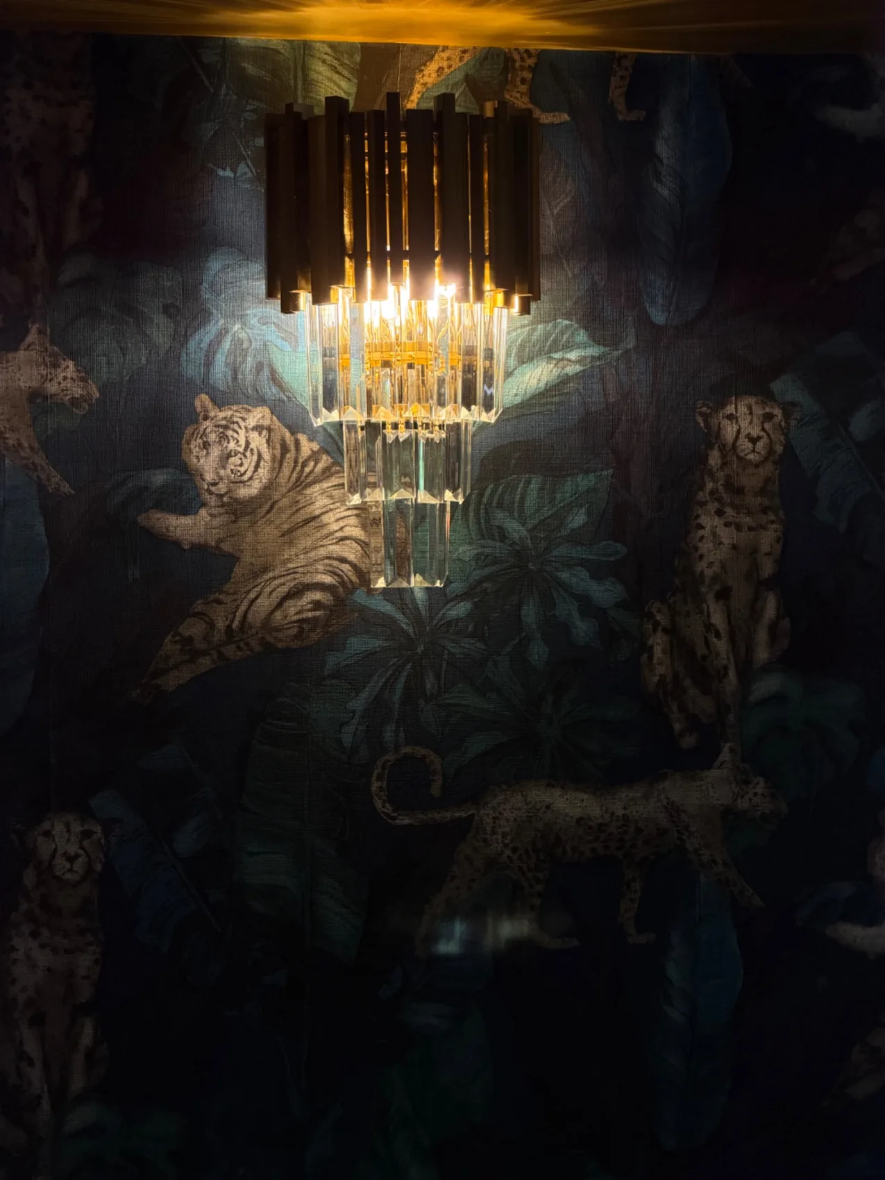 Warm crystal wall light against dramatic botanical wallpaper