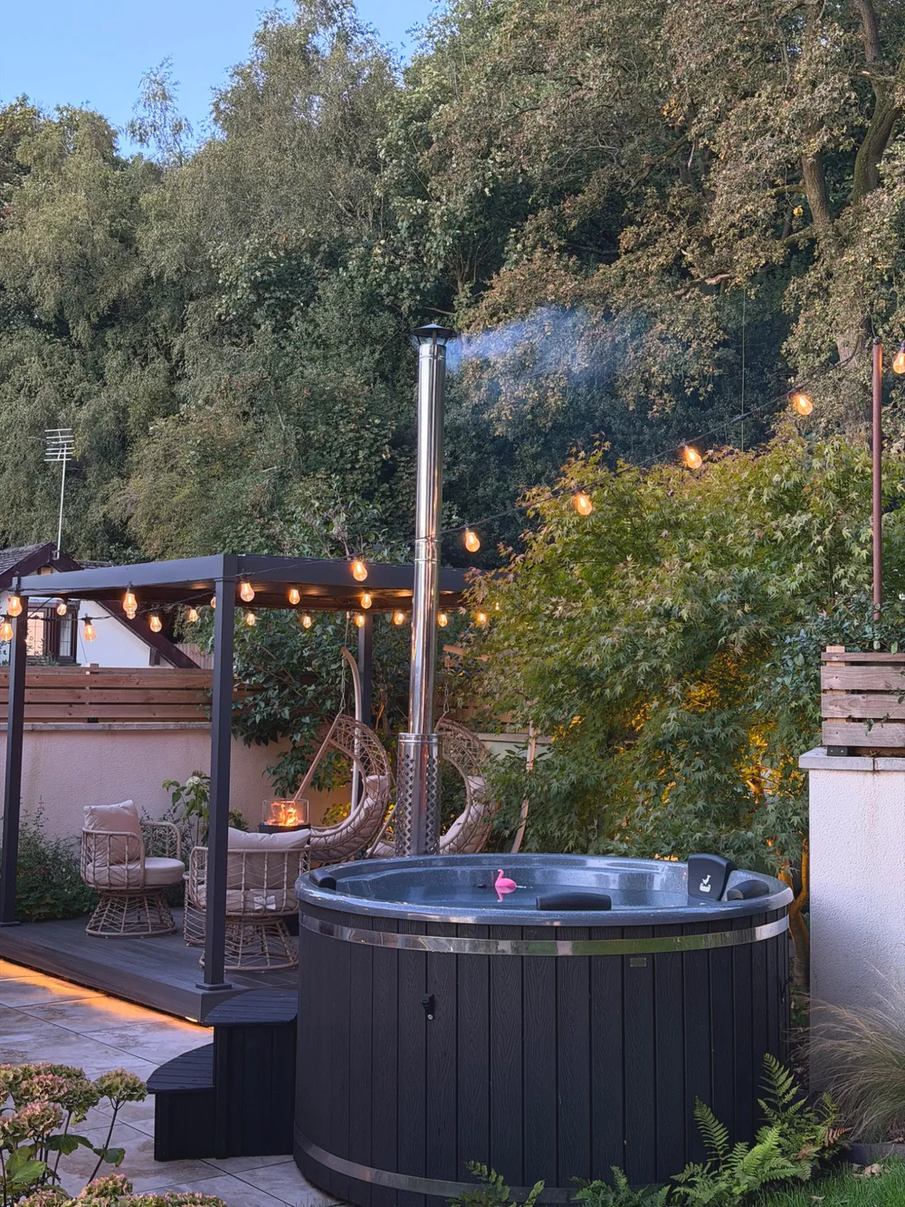 Wood-fired hot tub beside a softly lit outdoor seating area