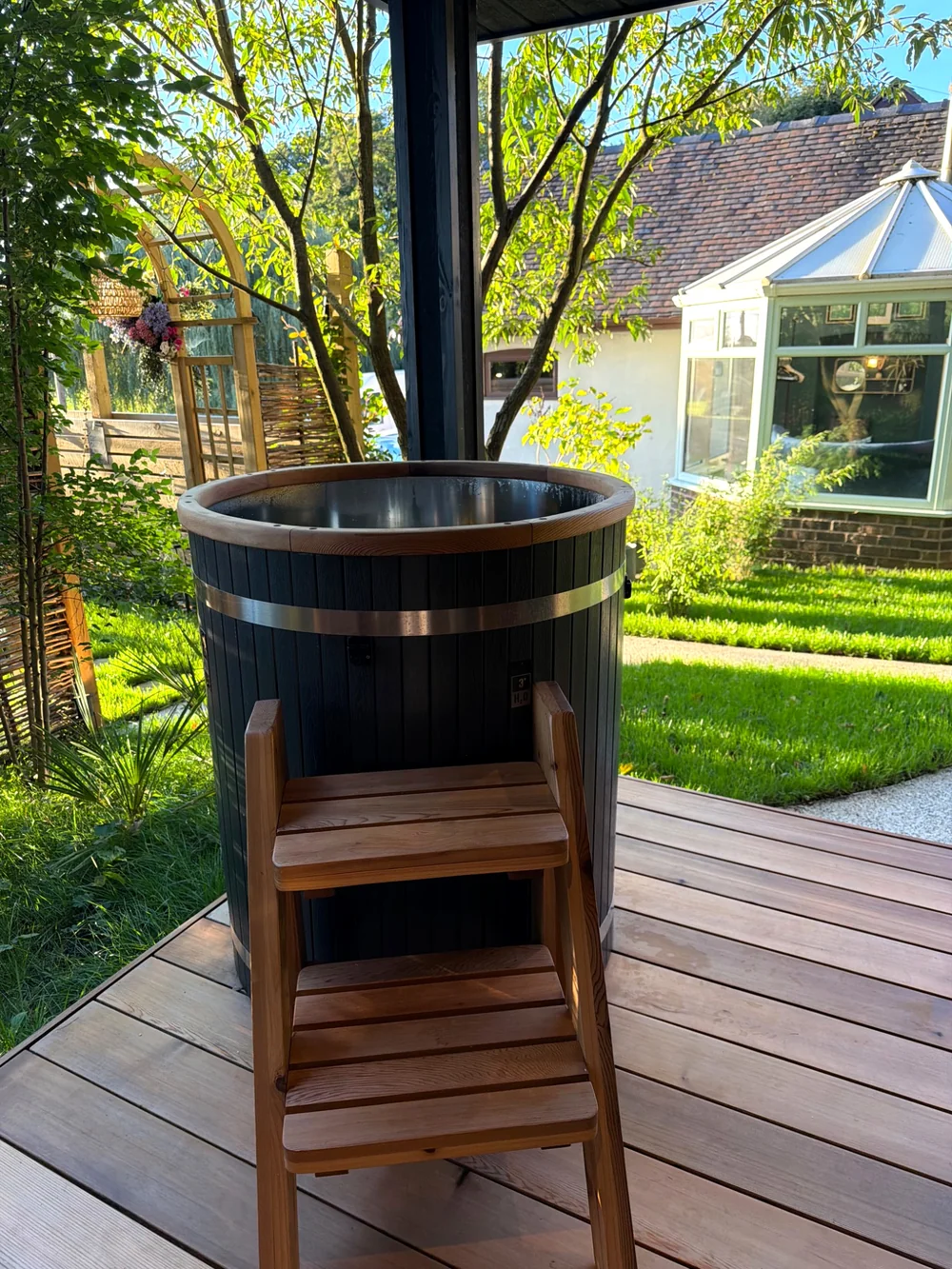 Outdoor wooden cold plunge pool on a deck beside the garden